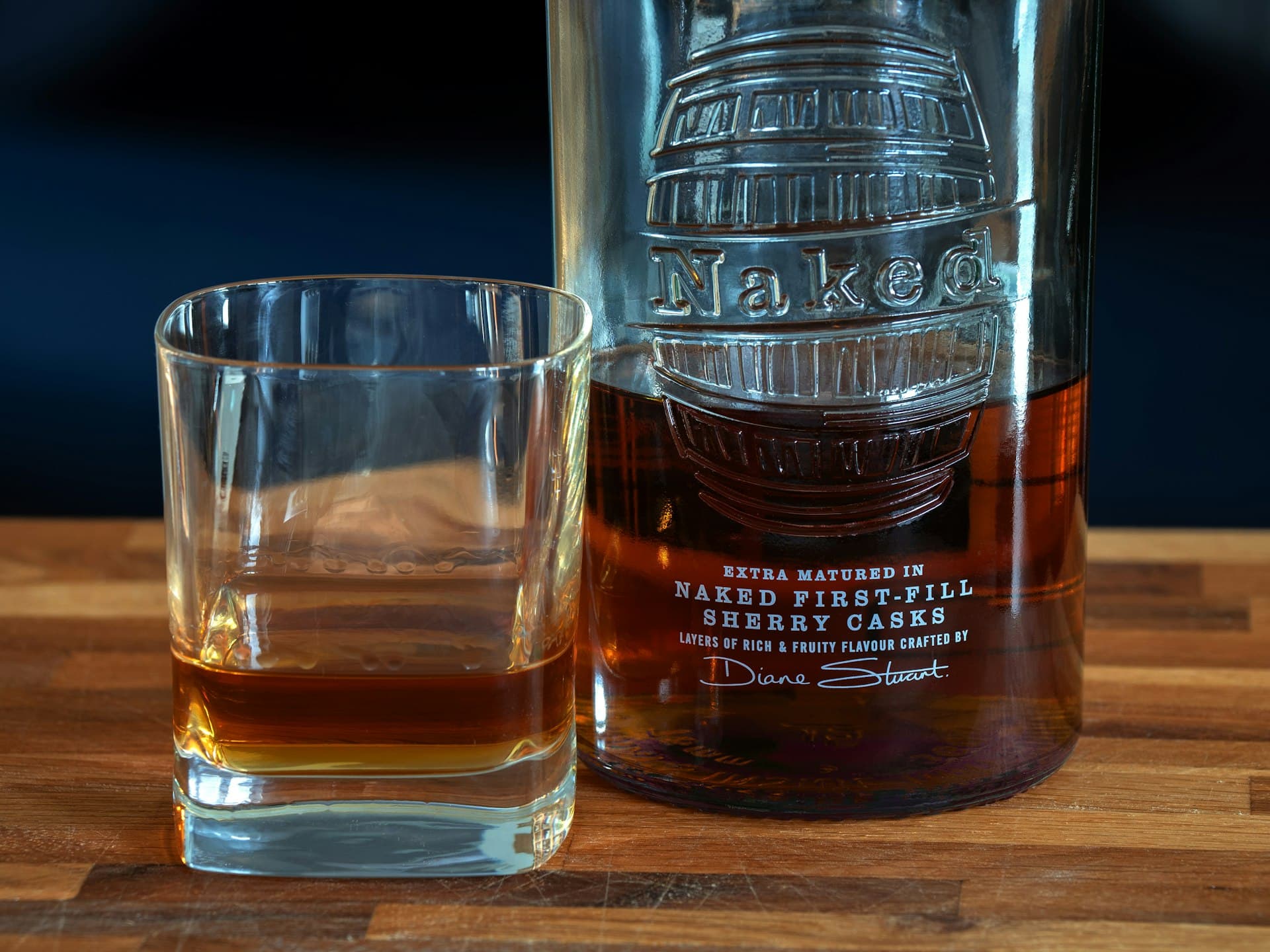 A whiskey glass on a dark wooden table, lit by warm light against a soft bokeh background