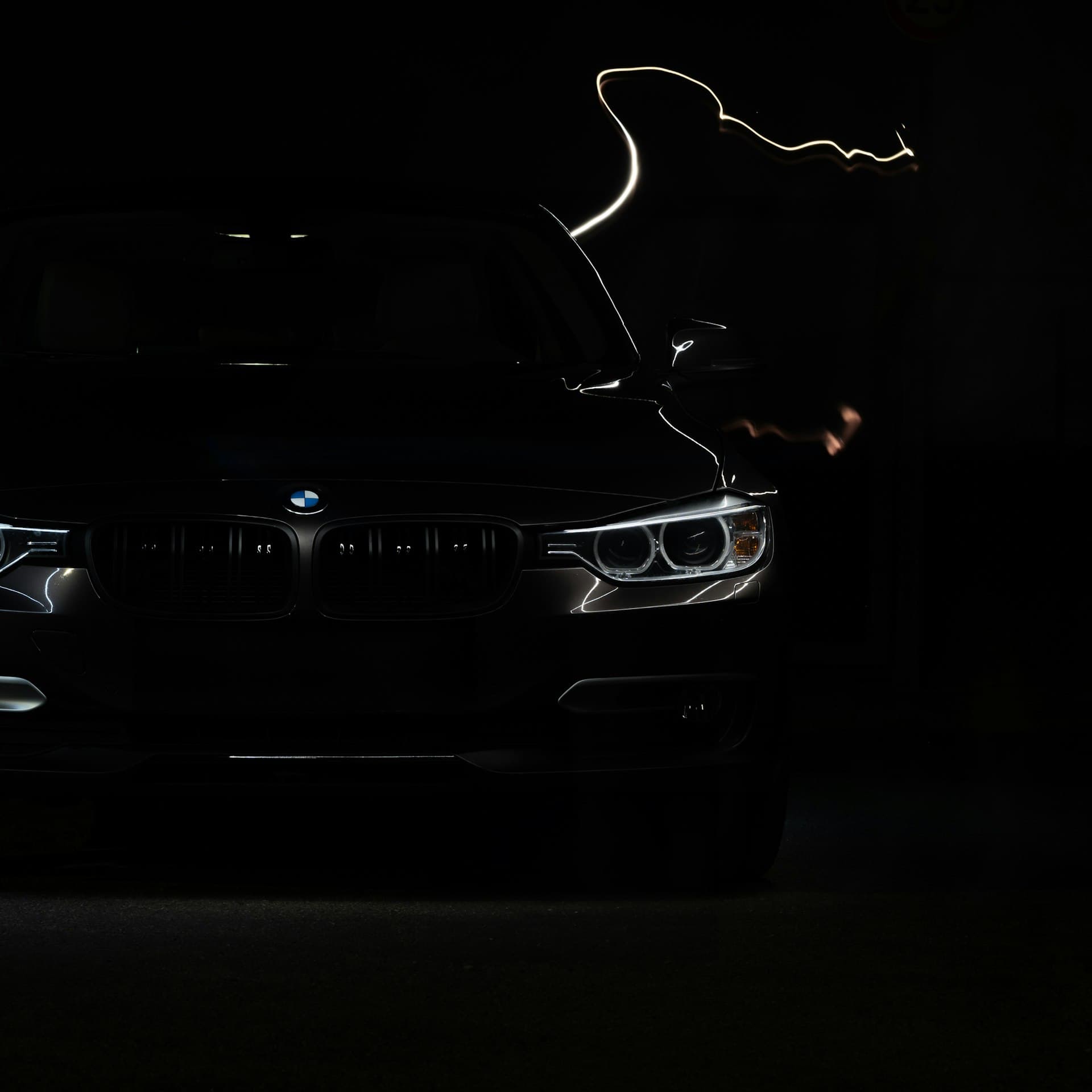 A black luxury car at night with its headlights illuminated against the darkness